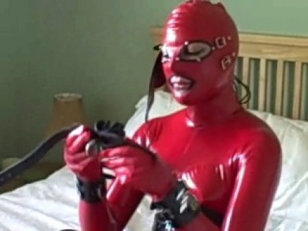 Latex Model Prepares For Work - Latex model arrives totally encased in latex.  Red latex catsuit and hood with latex corset and latex boots!

she is shown where the shoot will take place and the items she is to wear.  When we first see her she already has the leather wrist cuffs on.  Ankle cuffs follow and a rubber gag the like of which she has never seen before.

this gag has two internal rubber gum shields that fit over her teeth and when the gag strap is tightened there is no way she can talk.  A blindfold will complete the outfit but there is no way she can fit it properly while wearing rubber gloves.

resting on the bed she falls ****** only to awaken to find that one wrist is already tied to the headboard.  Watch as her bondage is completed, including the blindfold.  She struggles, but the gag prevents any complaints, even when the photographer takes advantage of her vulnerable state.